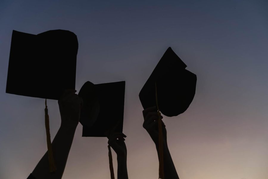 A picture of three hands holding up graduation camps at dusk
