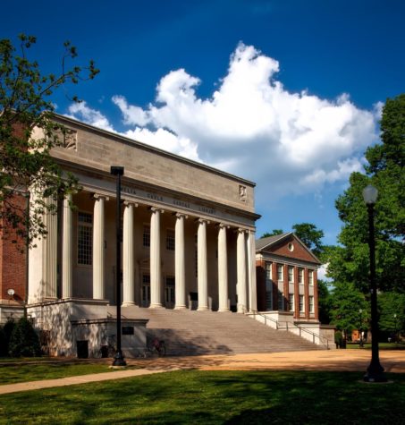 A college campus, somewhere, with a building with steps and columns and a sweeping green lawn and trees.